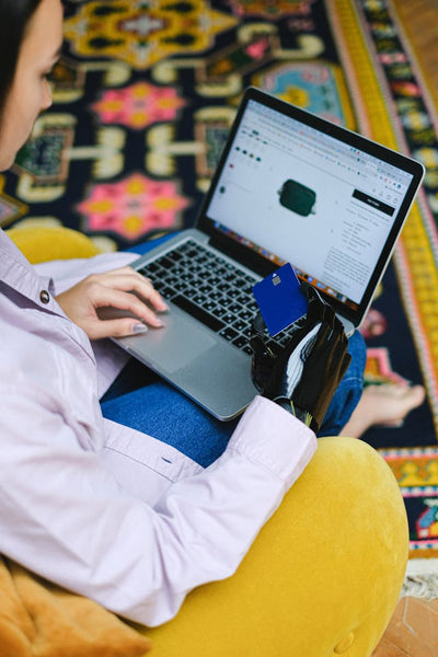 A woman with a prosthetic arm holds a credit card while online shopping on a laptop.