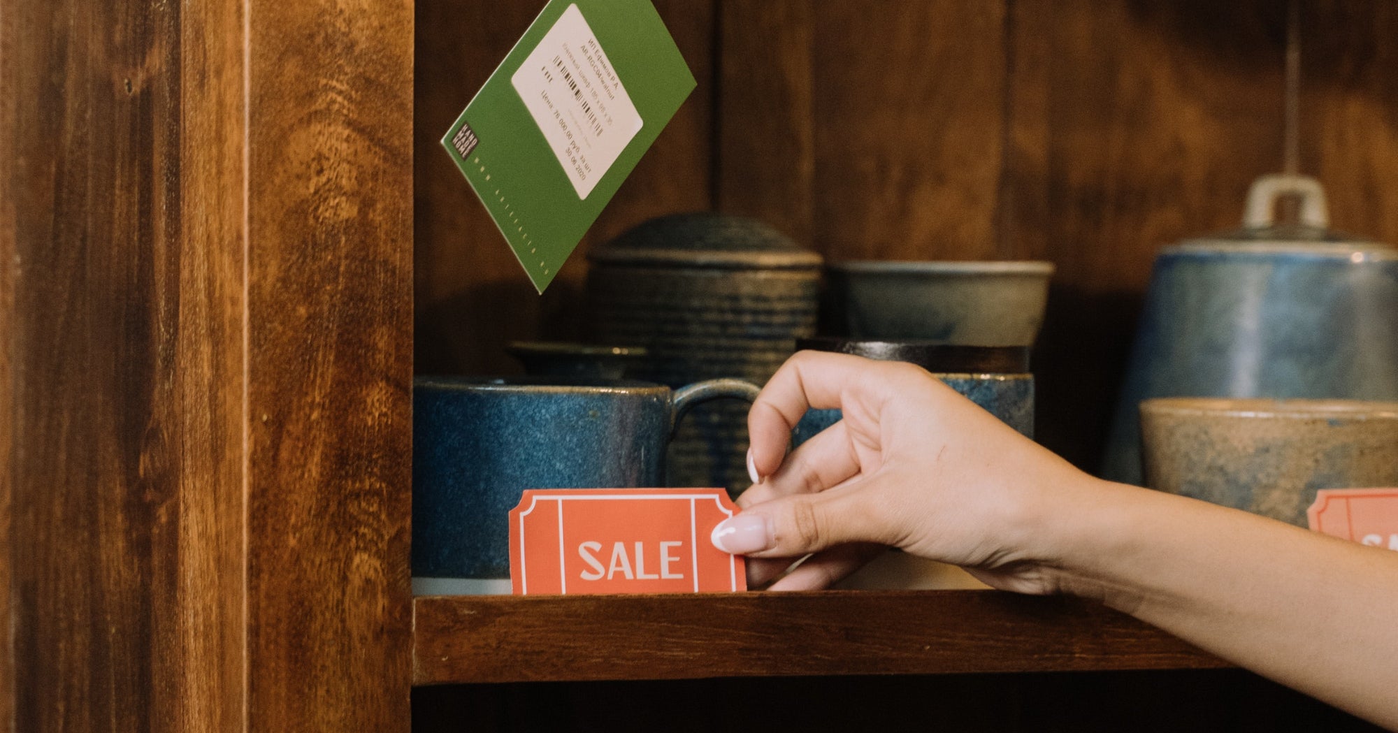 A hand places a sale tag on a shelf in a retail store