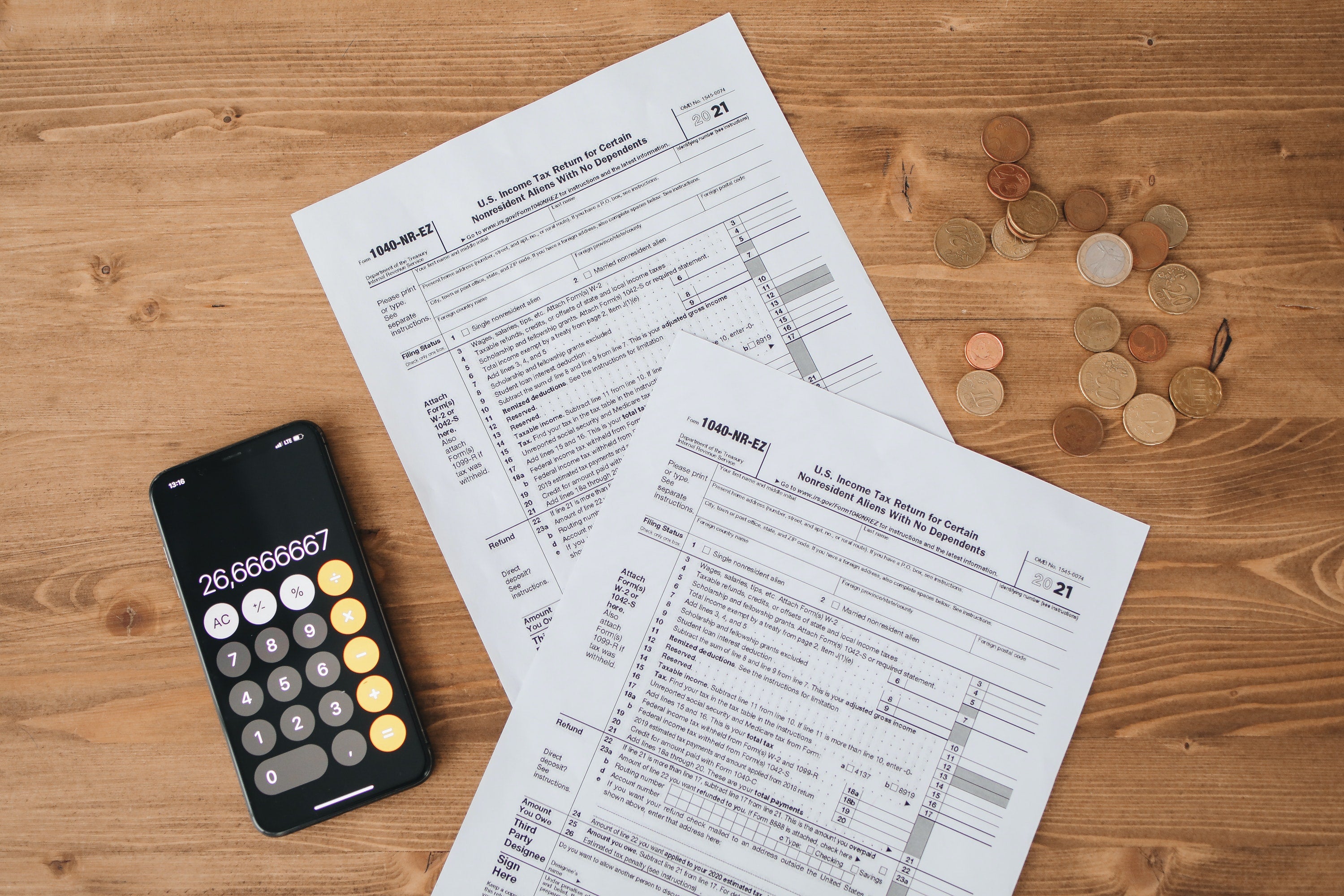 Two 1040 tax forms on a table next to a smartphone with the calculator app open