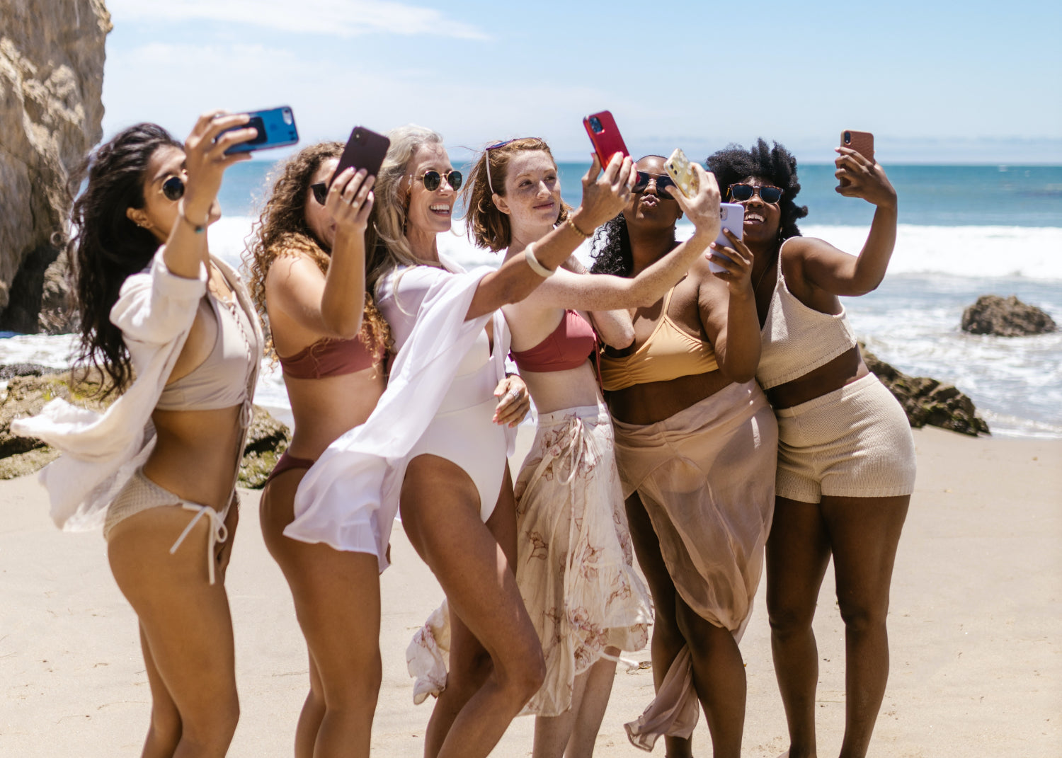 A row of women take selfies at the beach