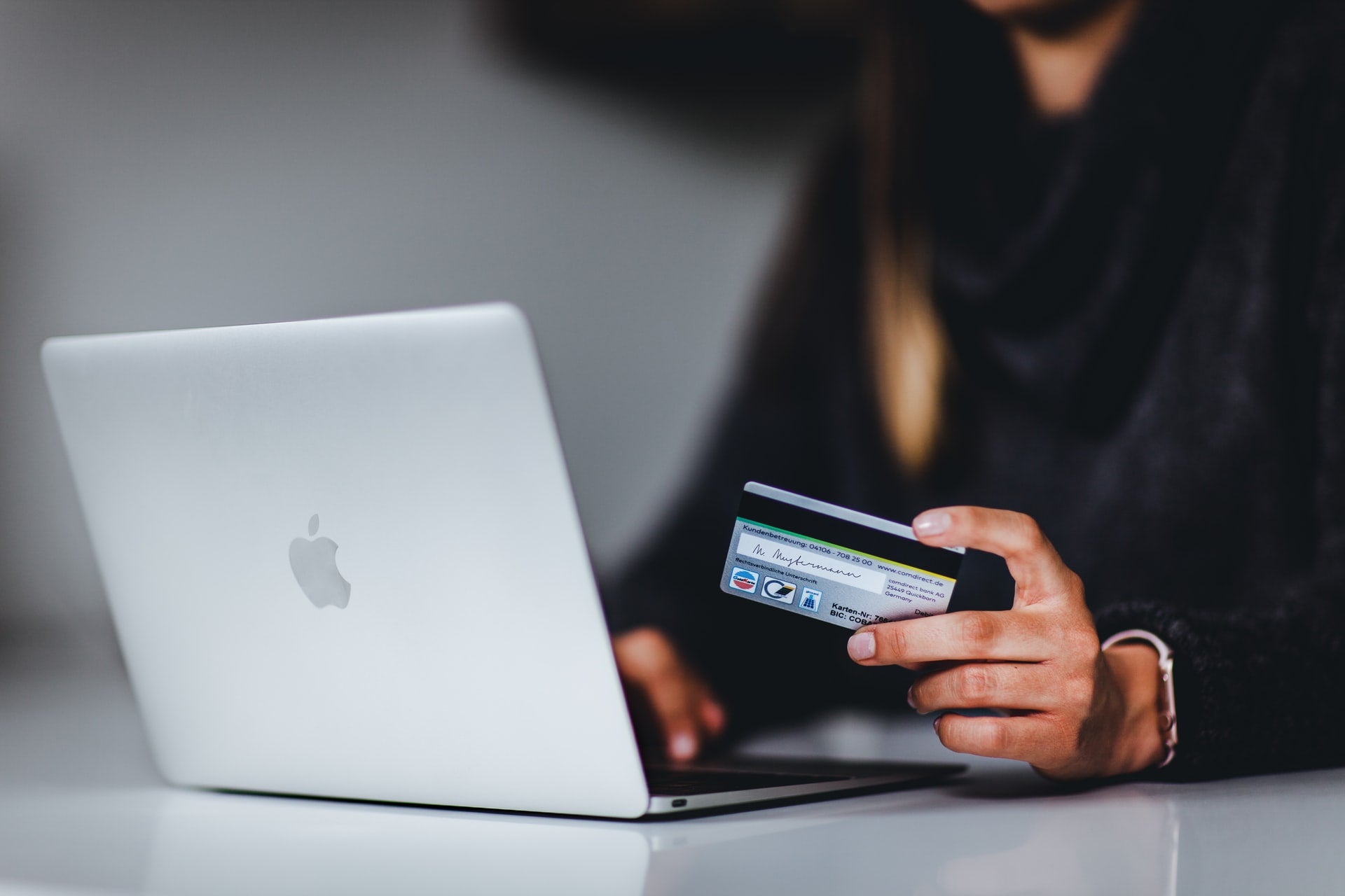 person looking at macbook, making an online purchase with credit card in left hand