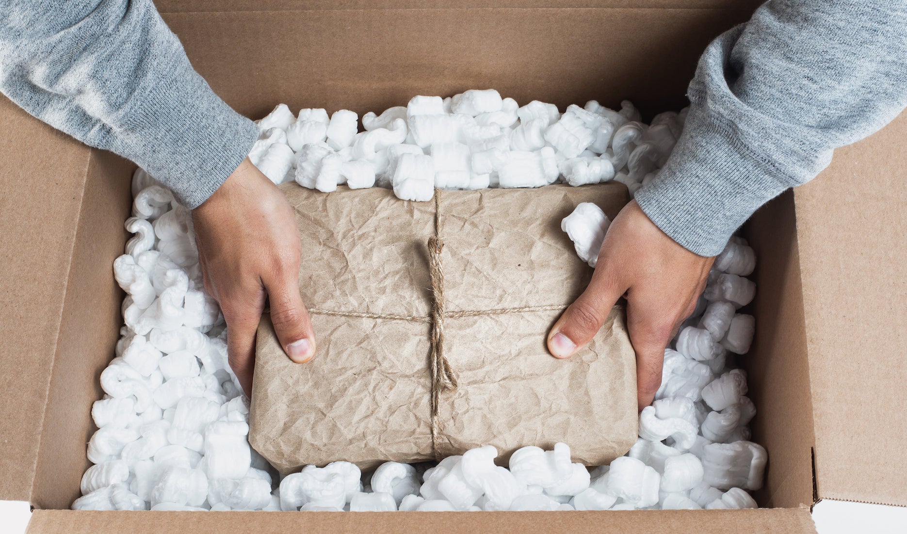 一双手在一只装满白色包装泡沫的纸箱里放进一个棕色包装纸包着的包裹