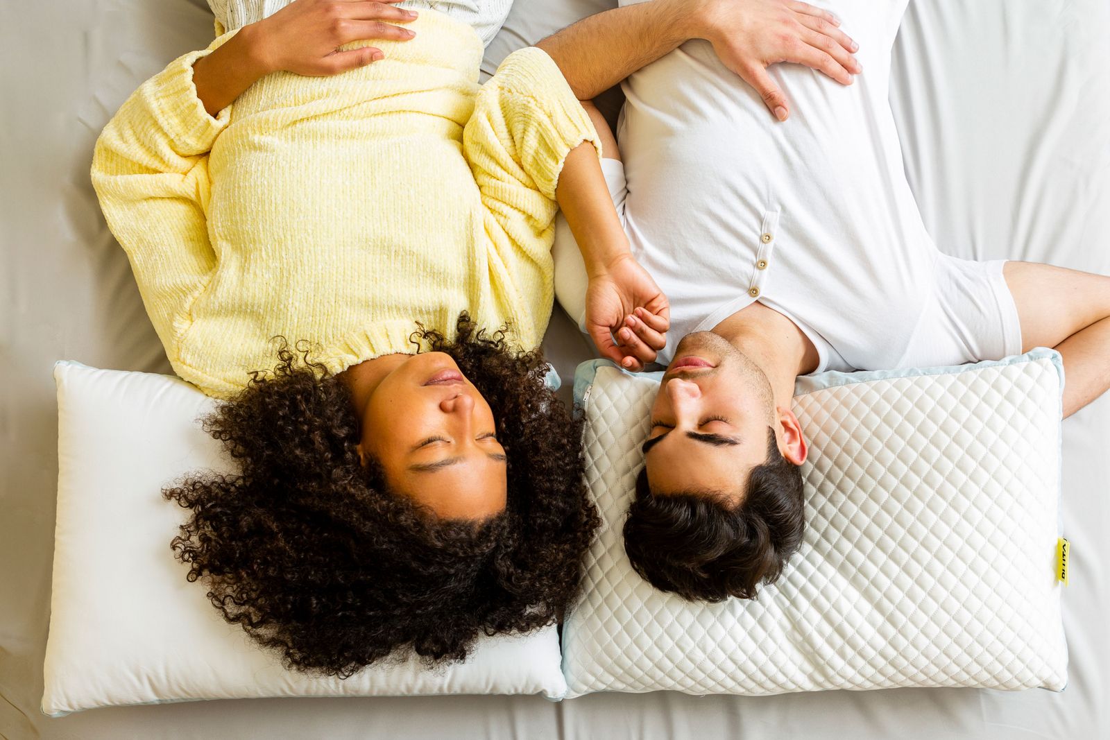 One woman (right) and one man (left) lying in bed, with their heads rested on two different Pluto Pillows.