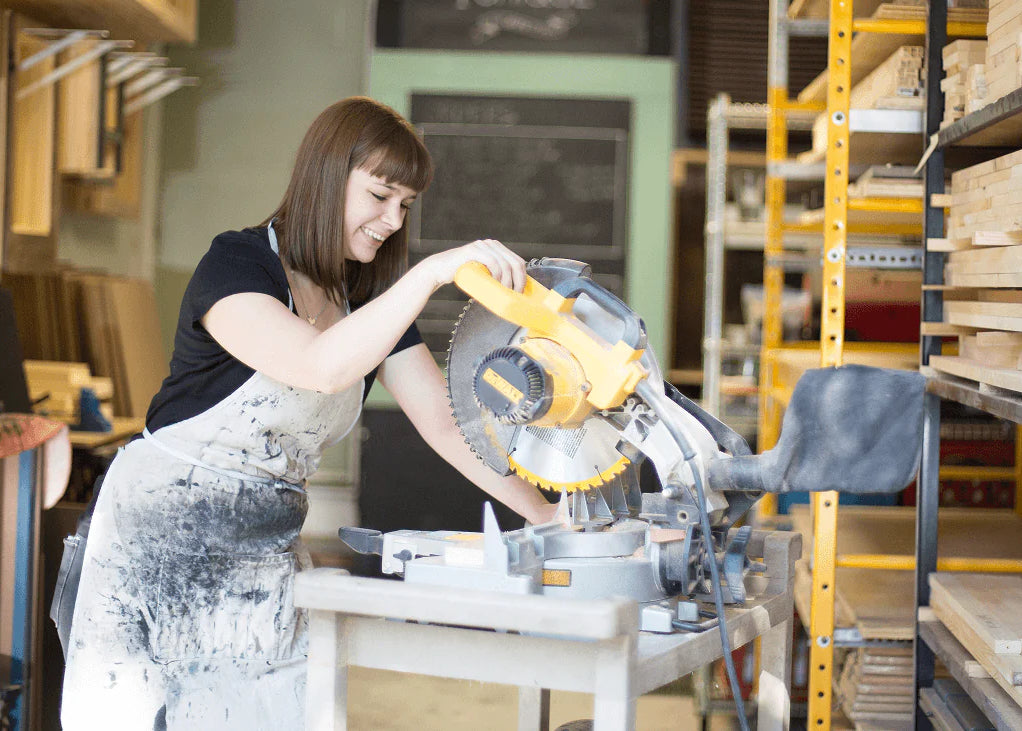 A woman uses a power saw in a workshop