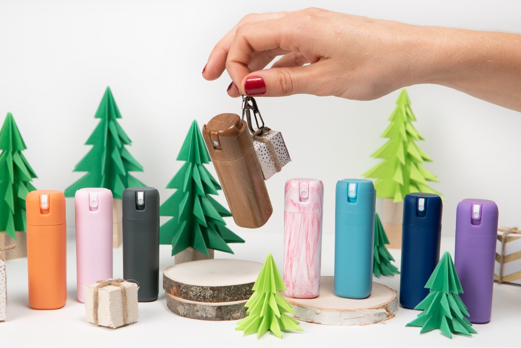 An array of Sanikind sanitizer dispensers in a faux forest setup while a hand model holds a capsule.