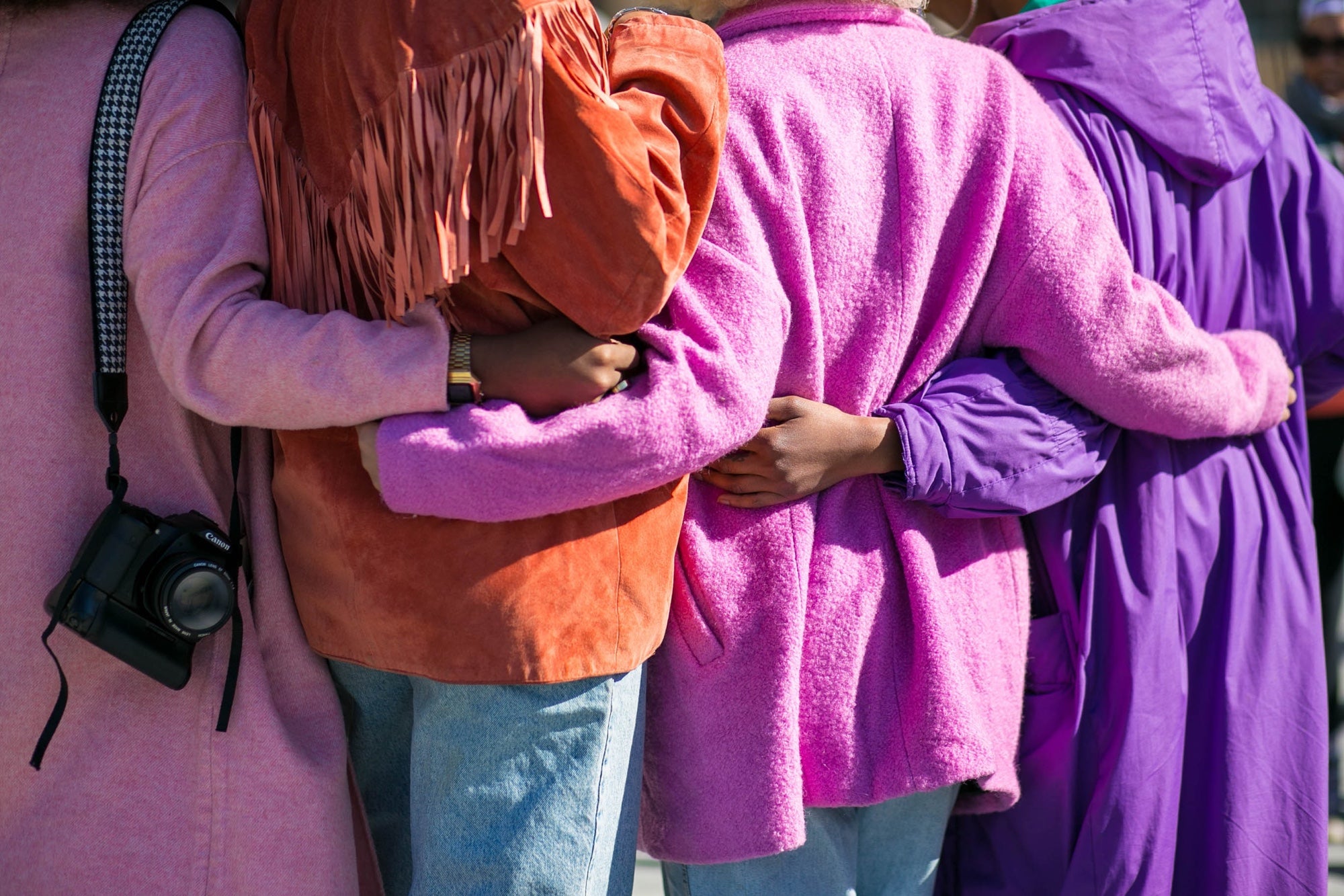 Shot from behind, a group of friends wrap their arms around each other