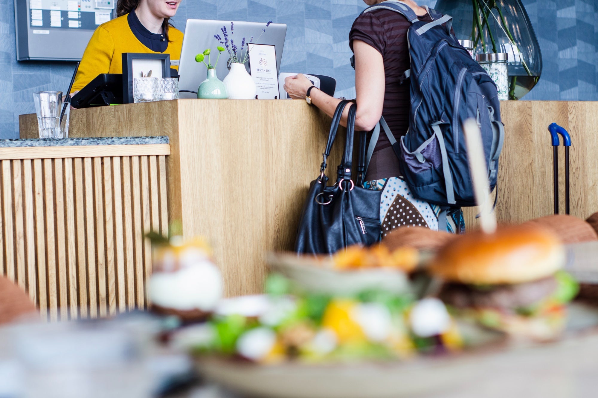 A person orders food in a coffee shop. A sandwich sits on a table in the foreground