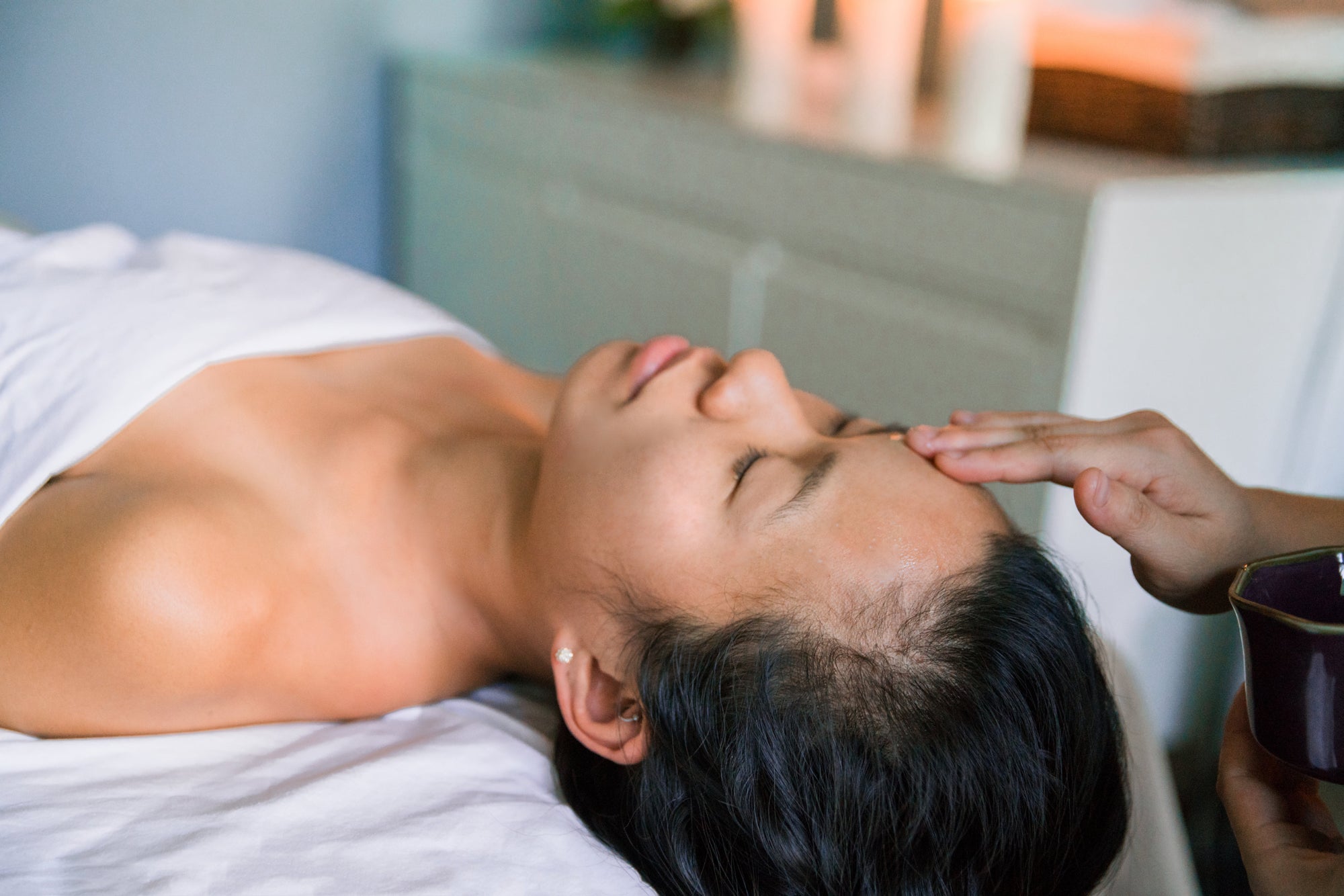 A person lies on a massage table while a therapist massages their head