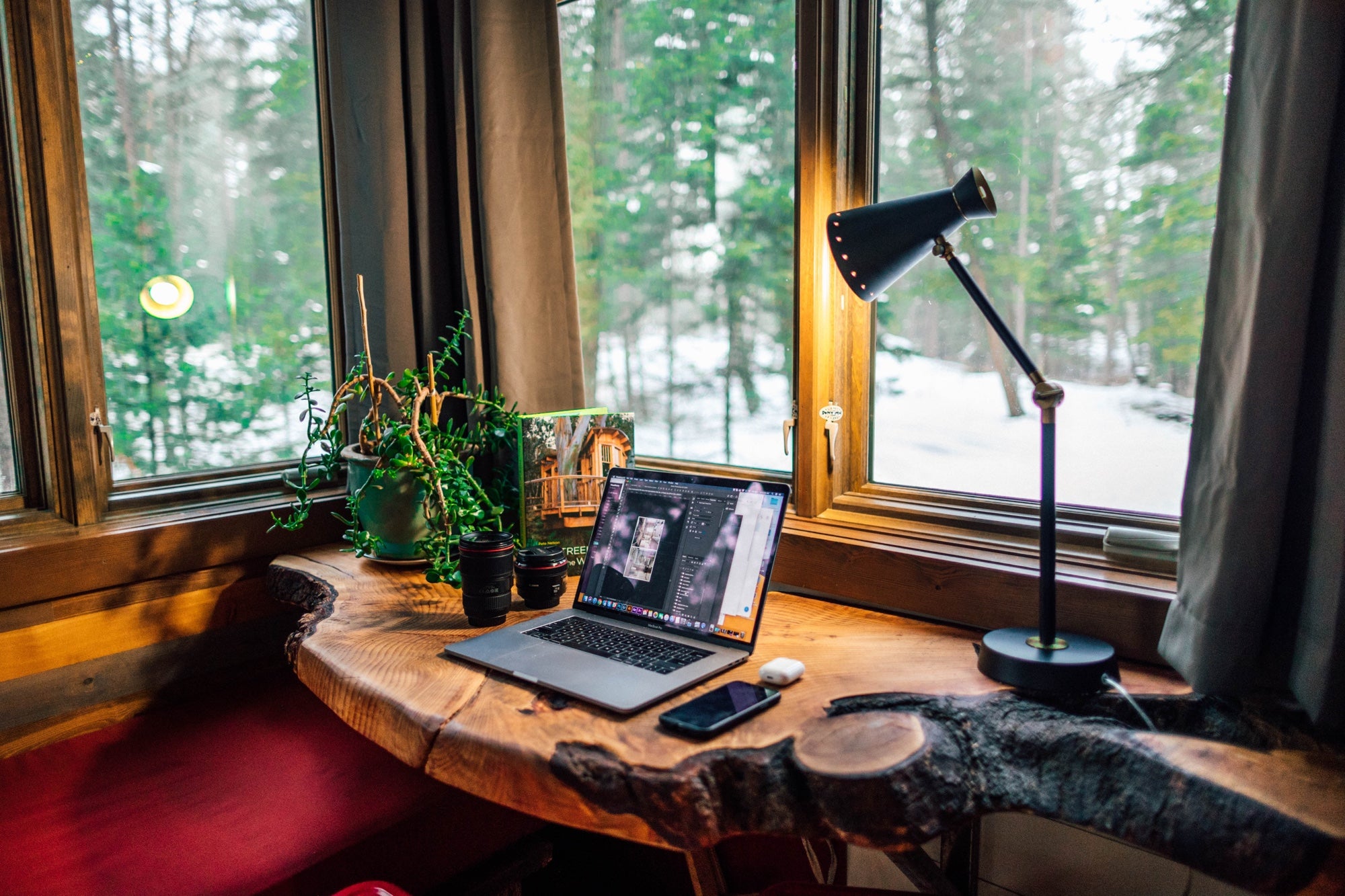 A home office in a cozy corner overlooking green space through wraparound windows