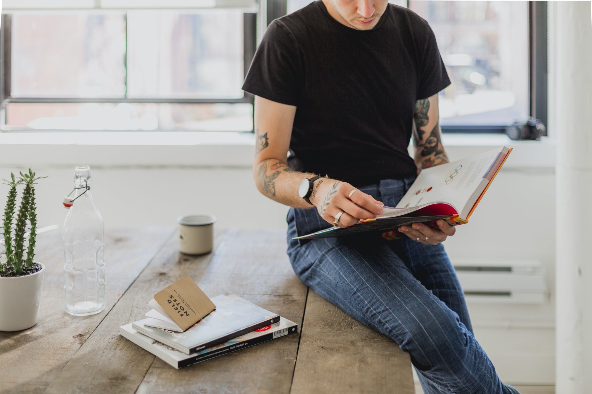 Man with tattoos sits on a table thumbing through a book