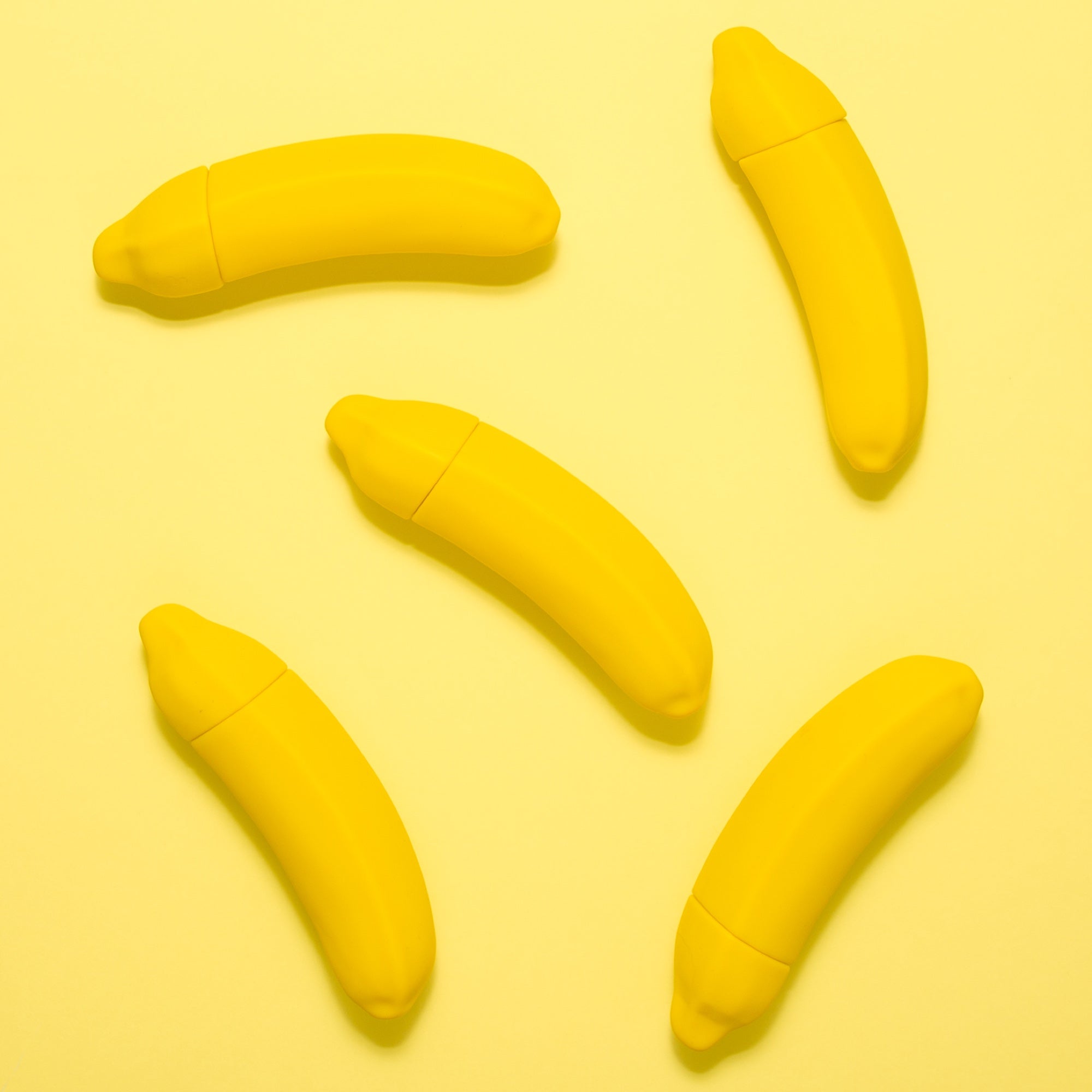 Fünf Vibratoren in Form einer Banane liegen auf einem gelben Hintergrund. Produktfotos sind wichtig, um Sexspielzeug zu verkaufen.
