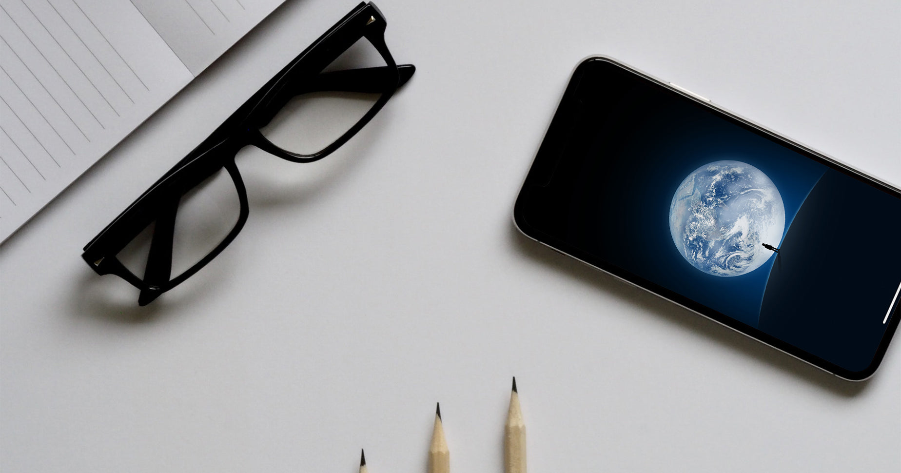 photo of desk with glasses, smartphone and pencils