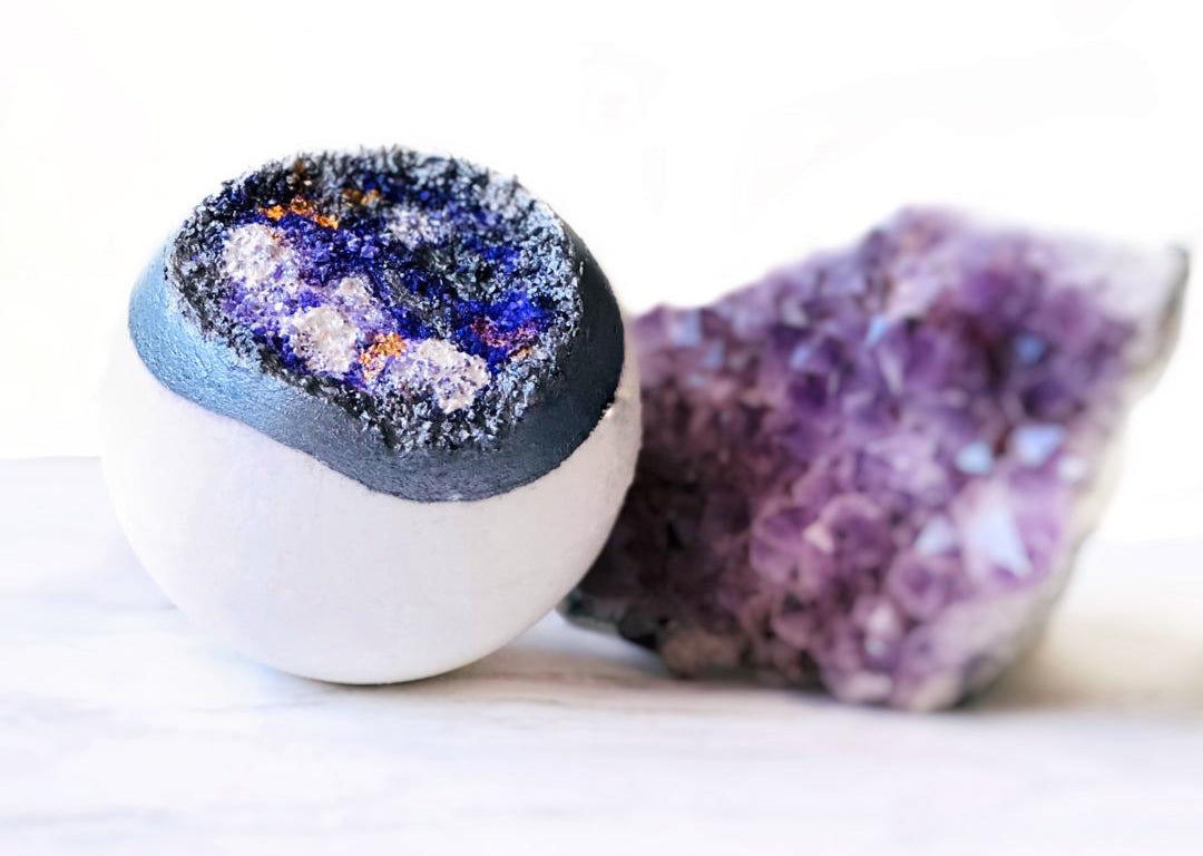 A bath bomb resembling a geode sits next to a colorful rock