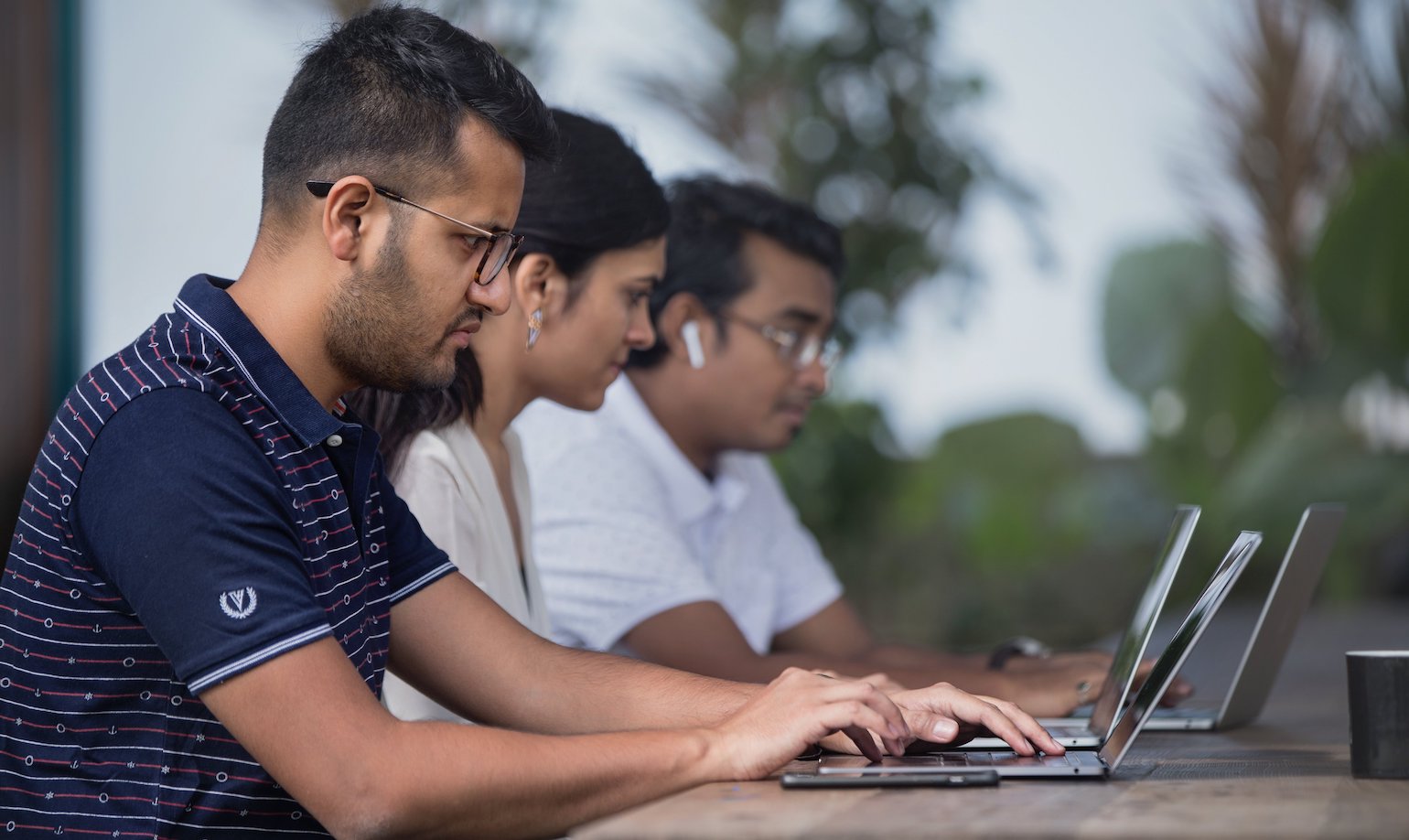 Three coworkers on laptops working together on a communal table. 