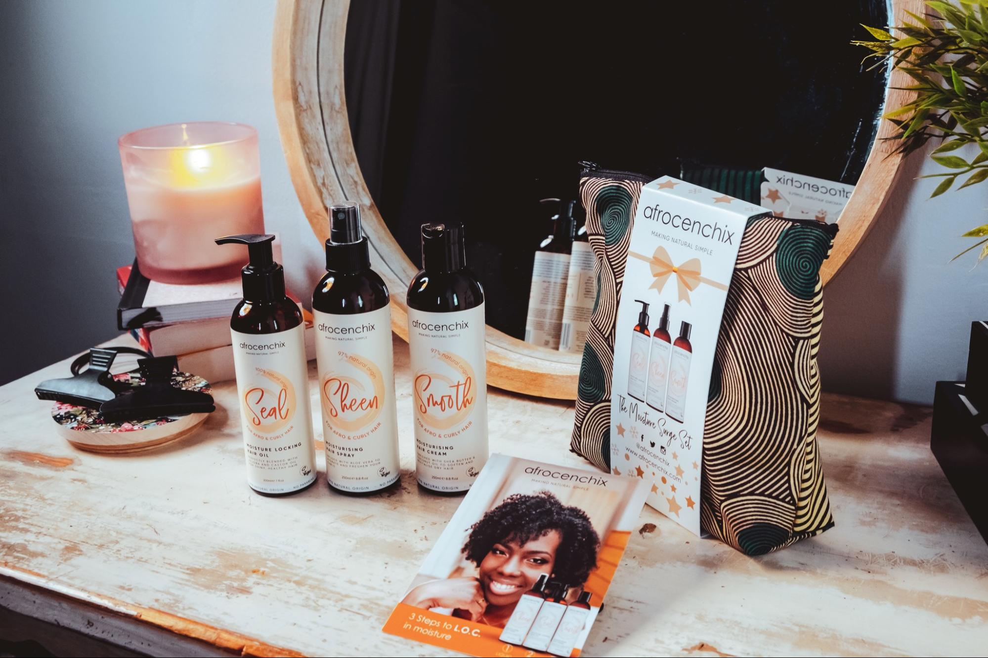 A selection of Afrocenchix products backdropped by a makeup back and mirror along with books and a candle. 