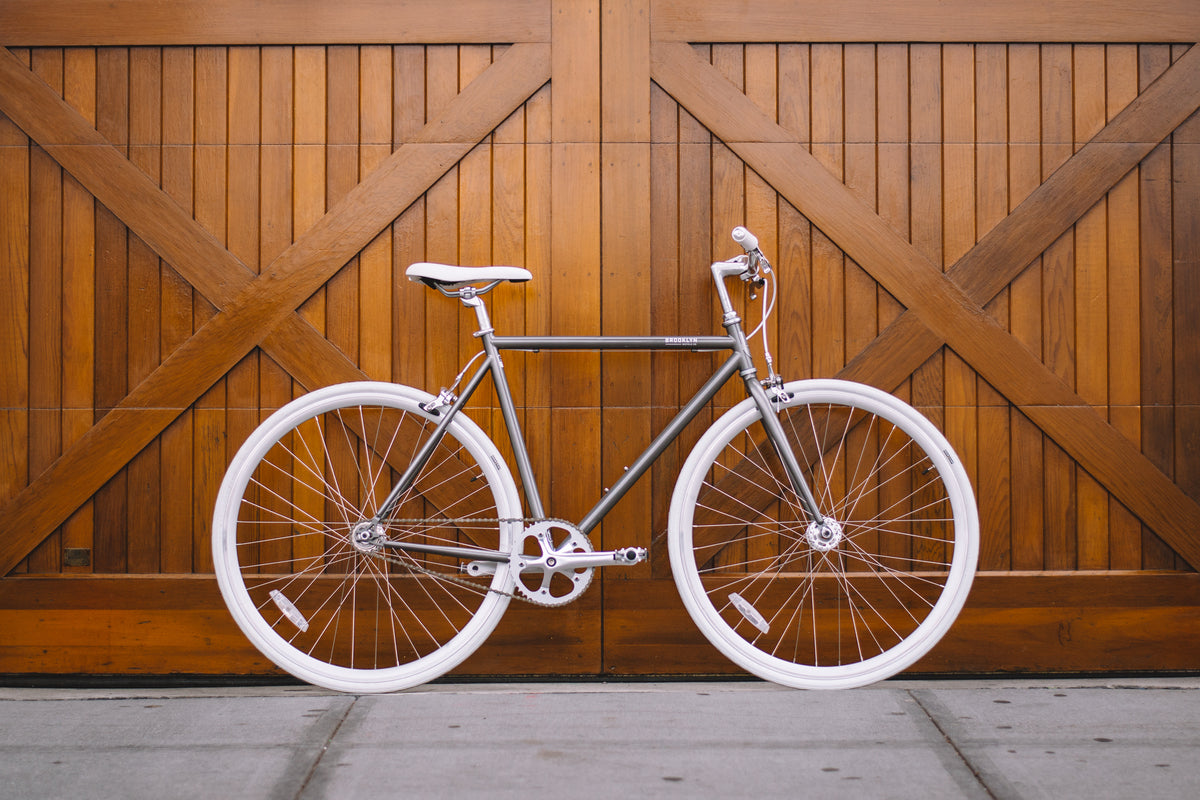 A bicycle by Brooklyn Bicycle Co. displayed against wooden doors and concrete floors. 