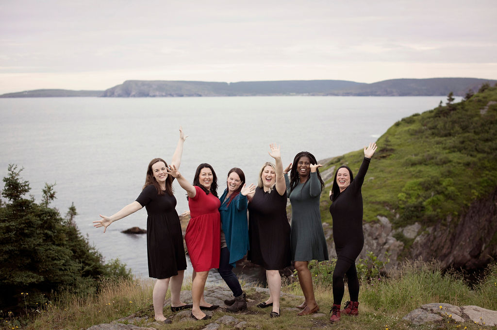 A group of five models wearing clothing from Buttercream Clothing backdropped by cliffs and ocean. 