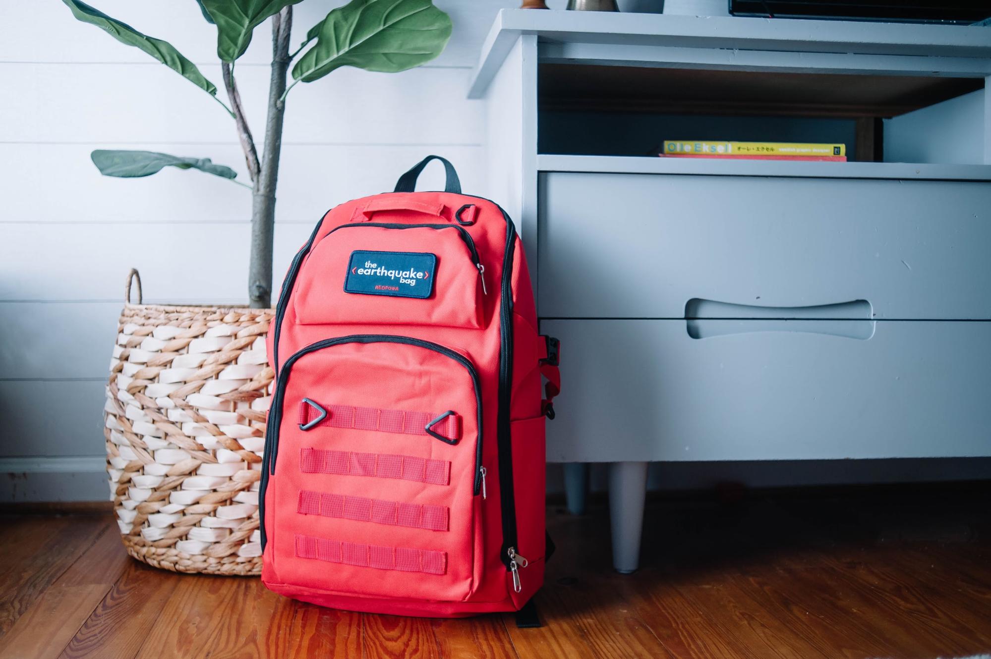 A Redfora earthquake preparedness backpack is backdropped by an end table and plant.