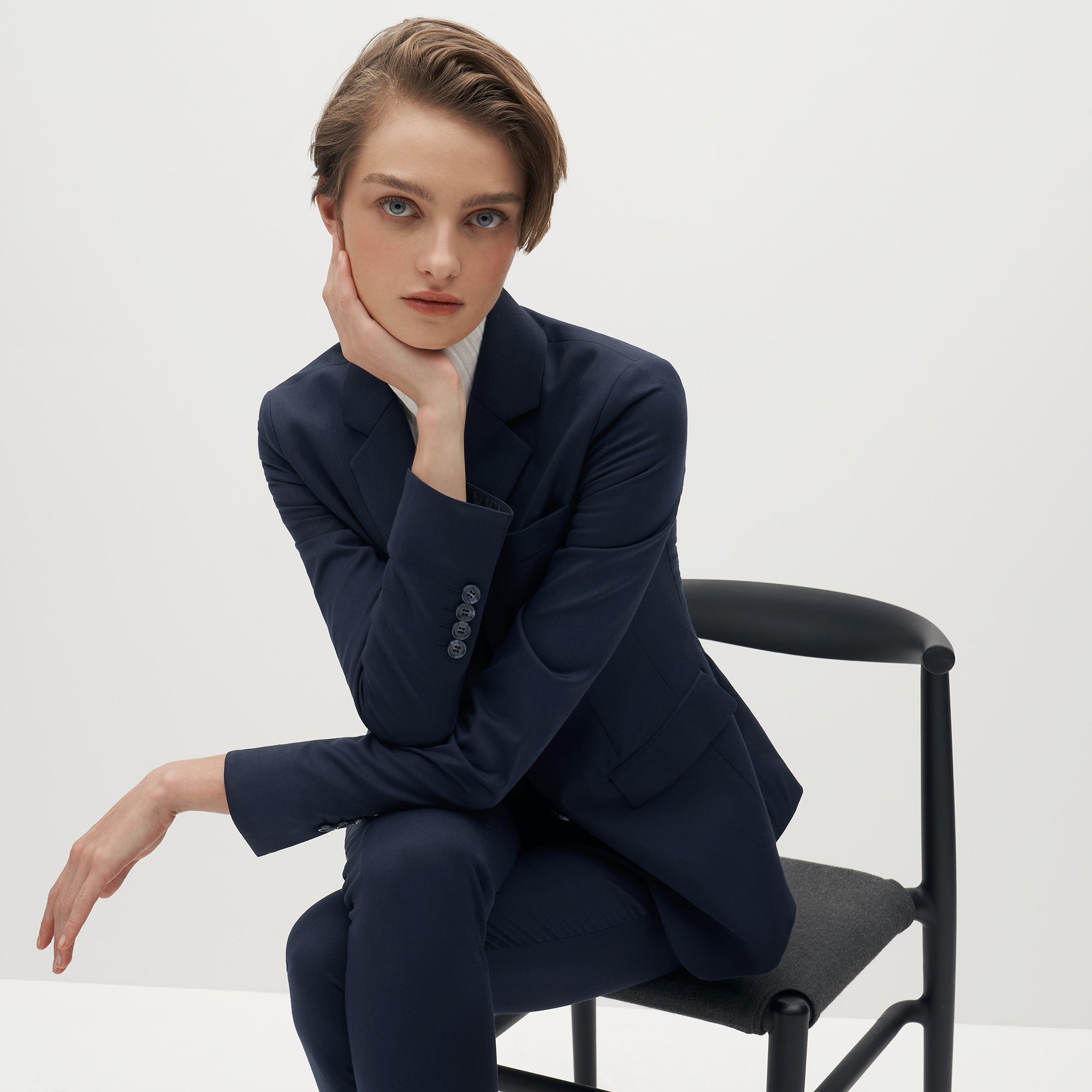 The Groomsman Suit: A female model wearing a navy suit sitting in a chair. 