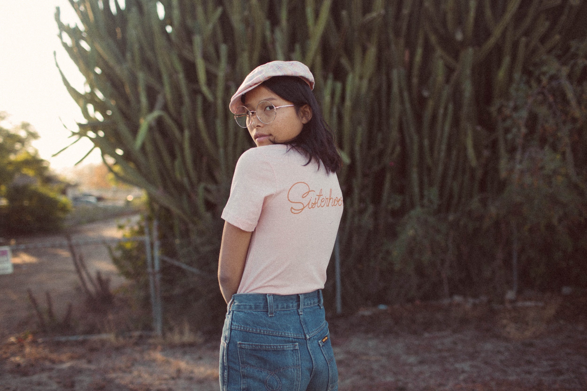 Image of a model wearing a hat and a t-shirt looking back over her shoulder against a background of trees