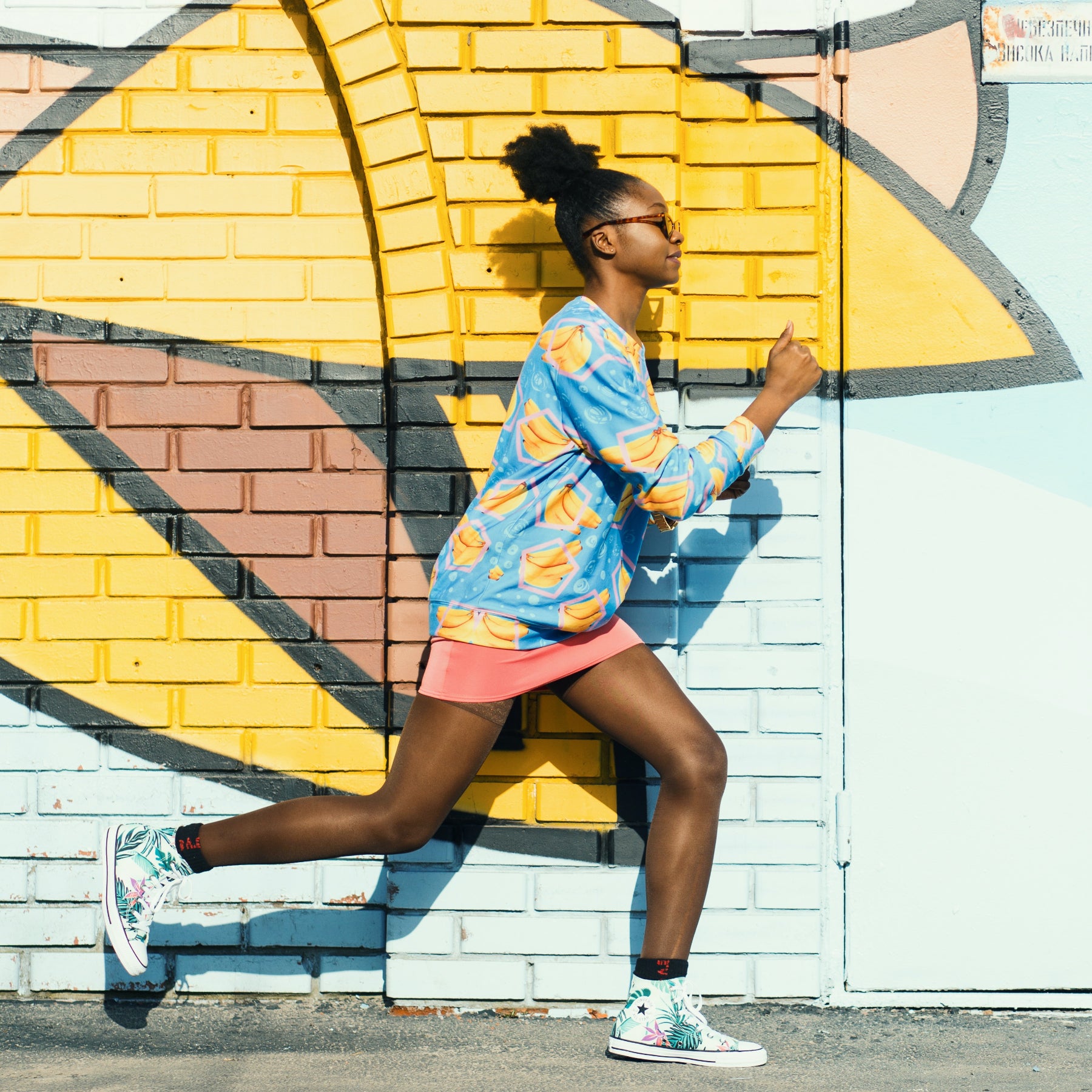 A young woman runs in front of a painted brick wall