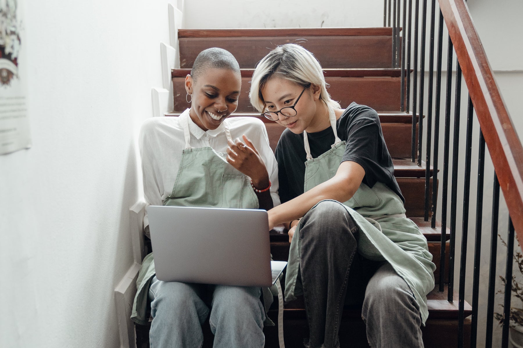 Two students sit on a stair looking at a laptop