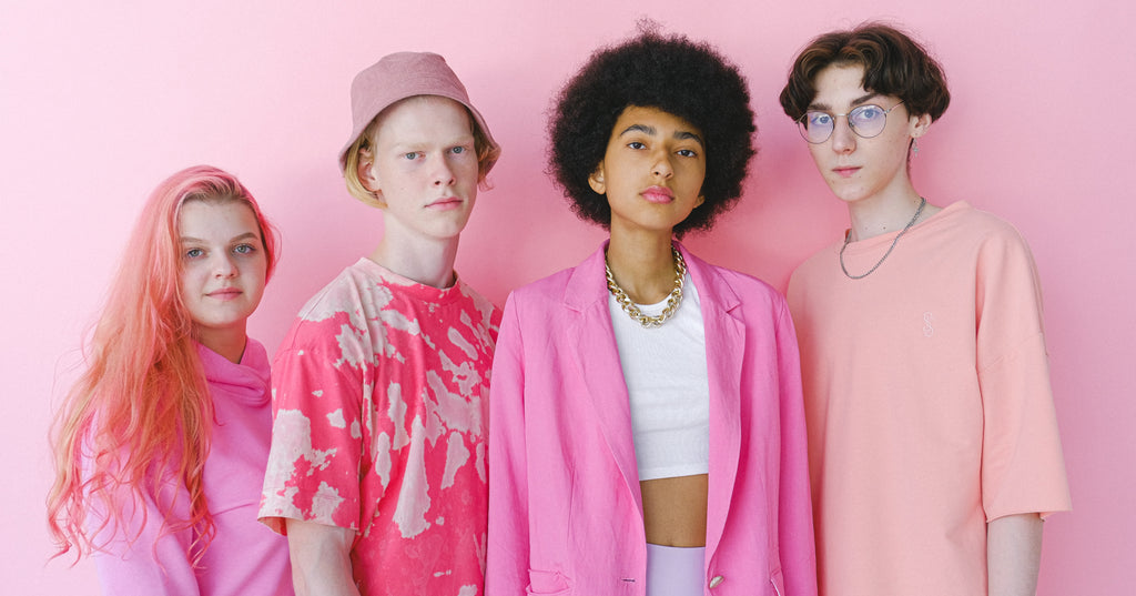A group of teens wearing pink stand against a pink background