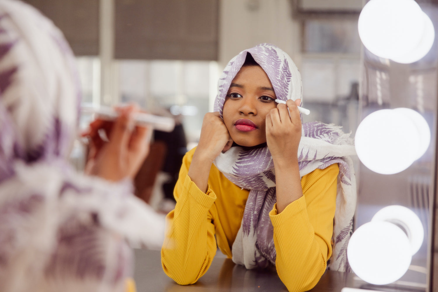 A woman does her makeup in front of a mirror in a professional studio