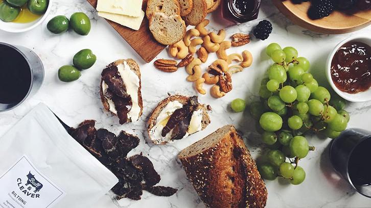 A food spread on a table including grapes, nuts and biltong 