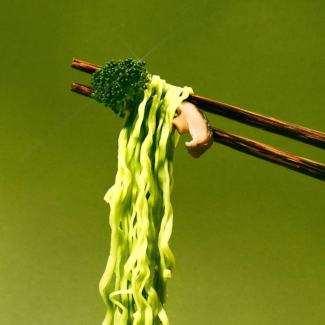Close up of chopsticks picking up green noodles