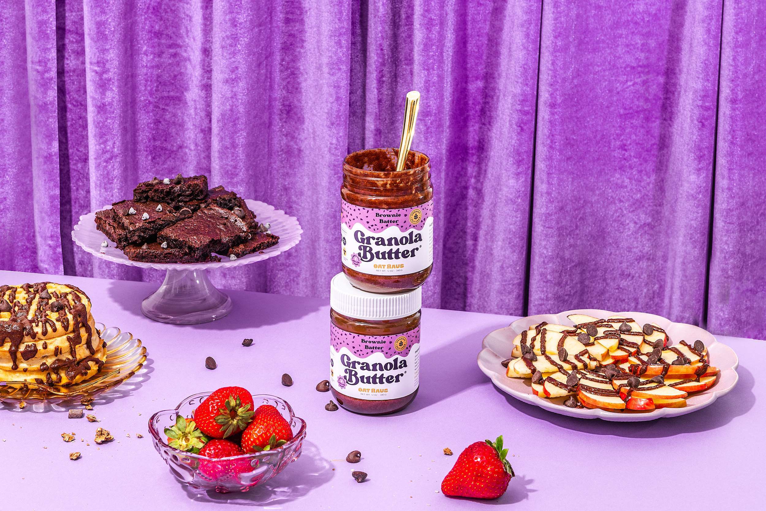 Oat Haus products styled with other foods against a purple curtain