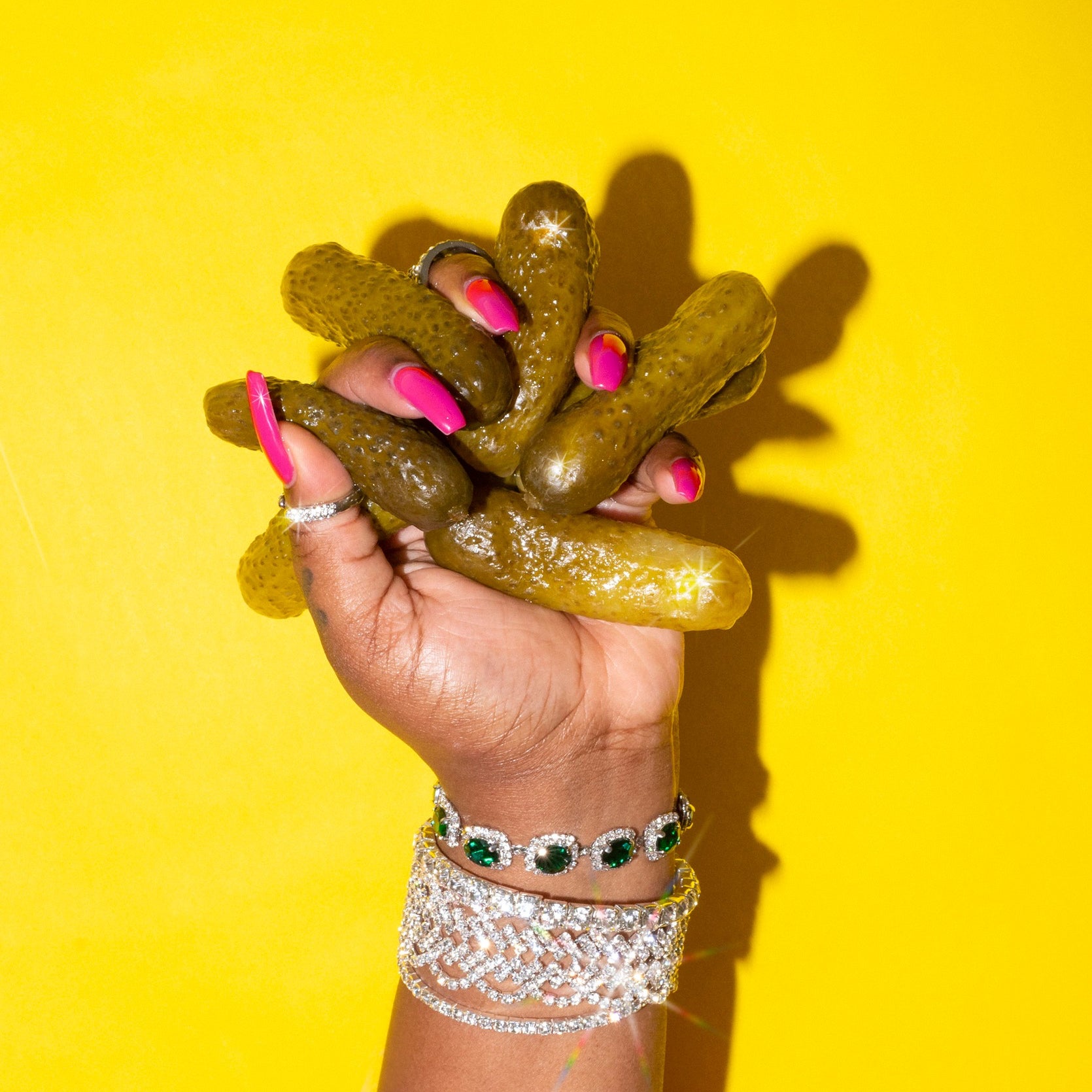 A hand with fancy jewelry holds a bunch of cucumber pickles