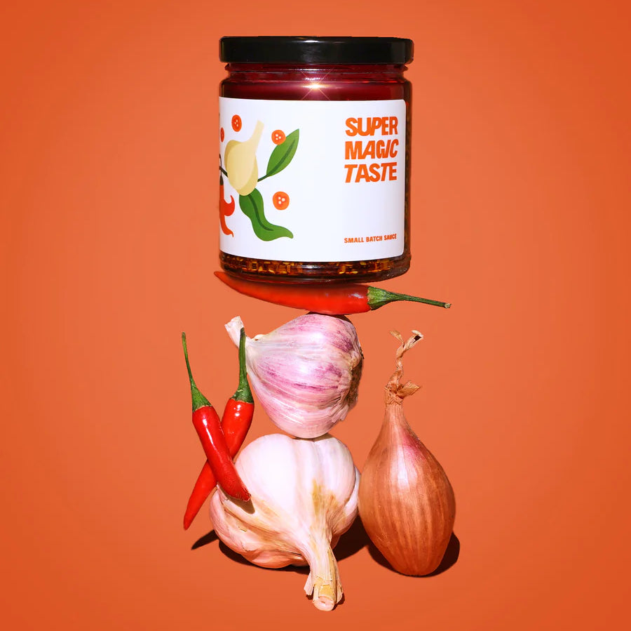 A jar of chilli oil is stacked atop garlic, shallots, and chilies