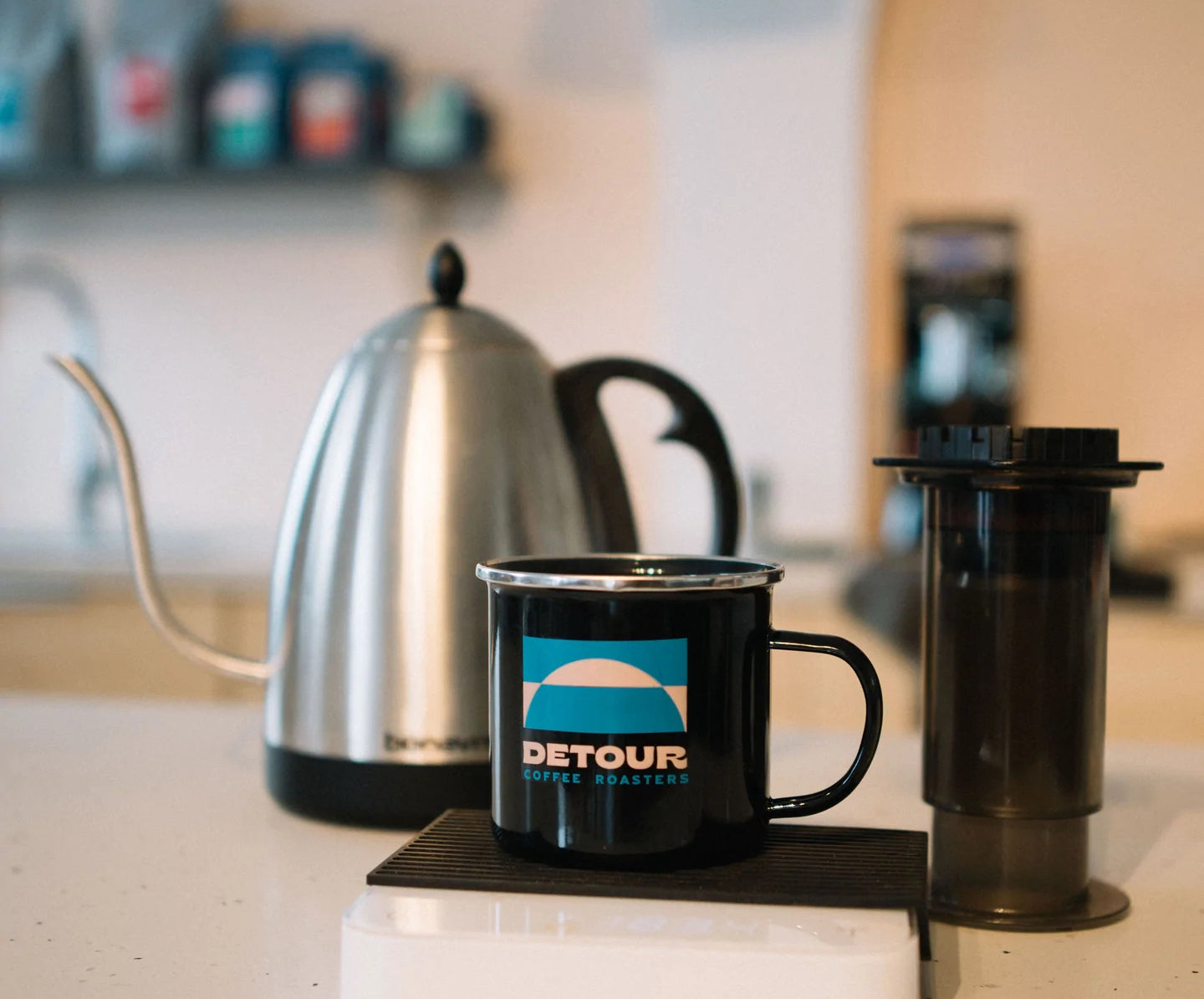 Coffee mug and kettle in a kitchen setting. Mug reads "detour"