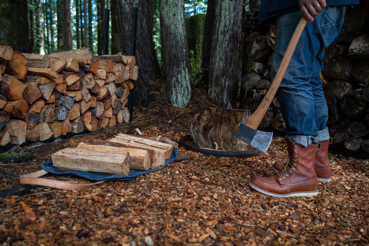 Person with an axe stands near a wood pile. 