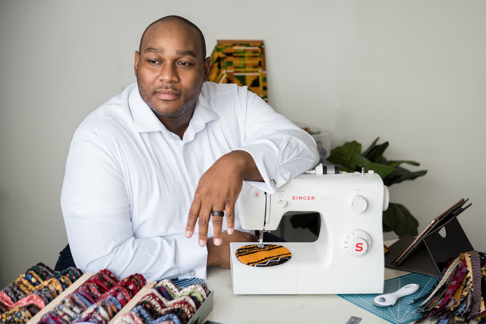 Terrell Grayson sits at a sewing machine with an array of bowties spread out before him