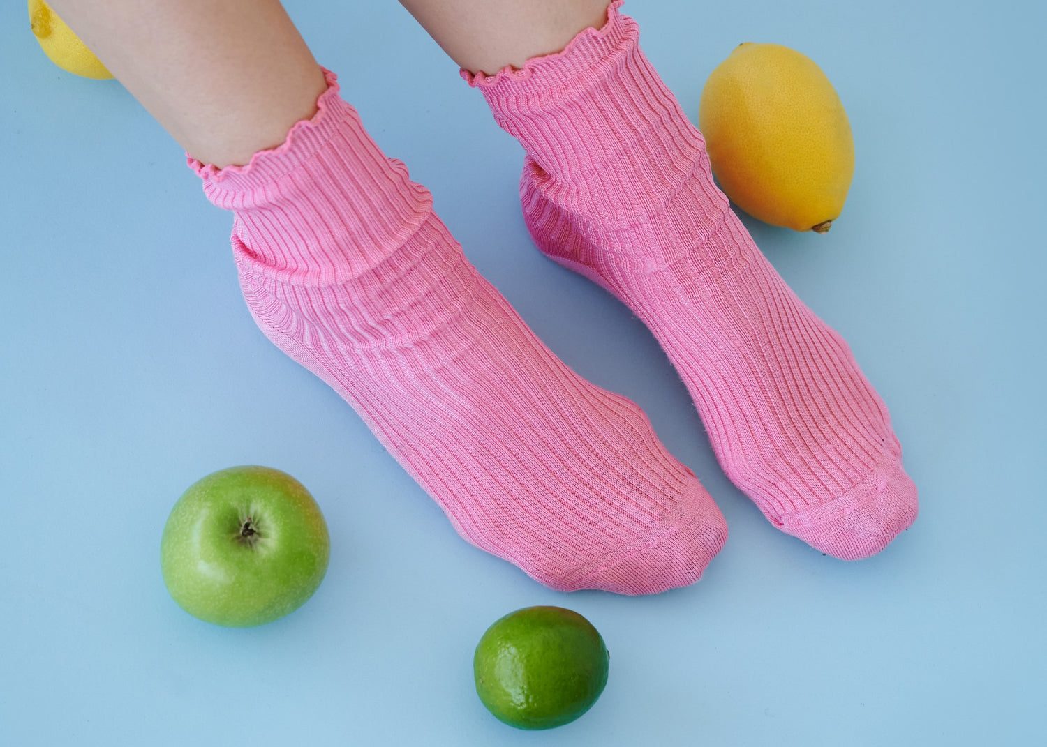 A pair of feet model pink socks and rest amongst limes and lemons