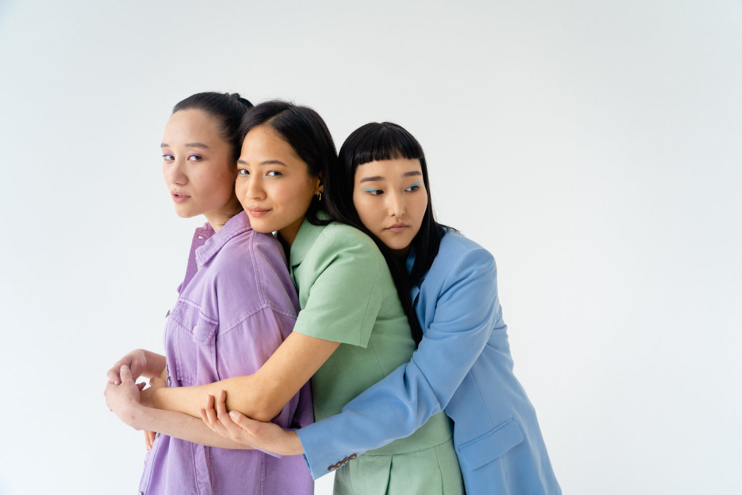 Three people in pastel suits hug together in a line