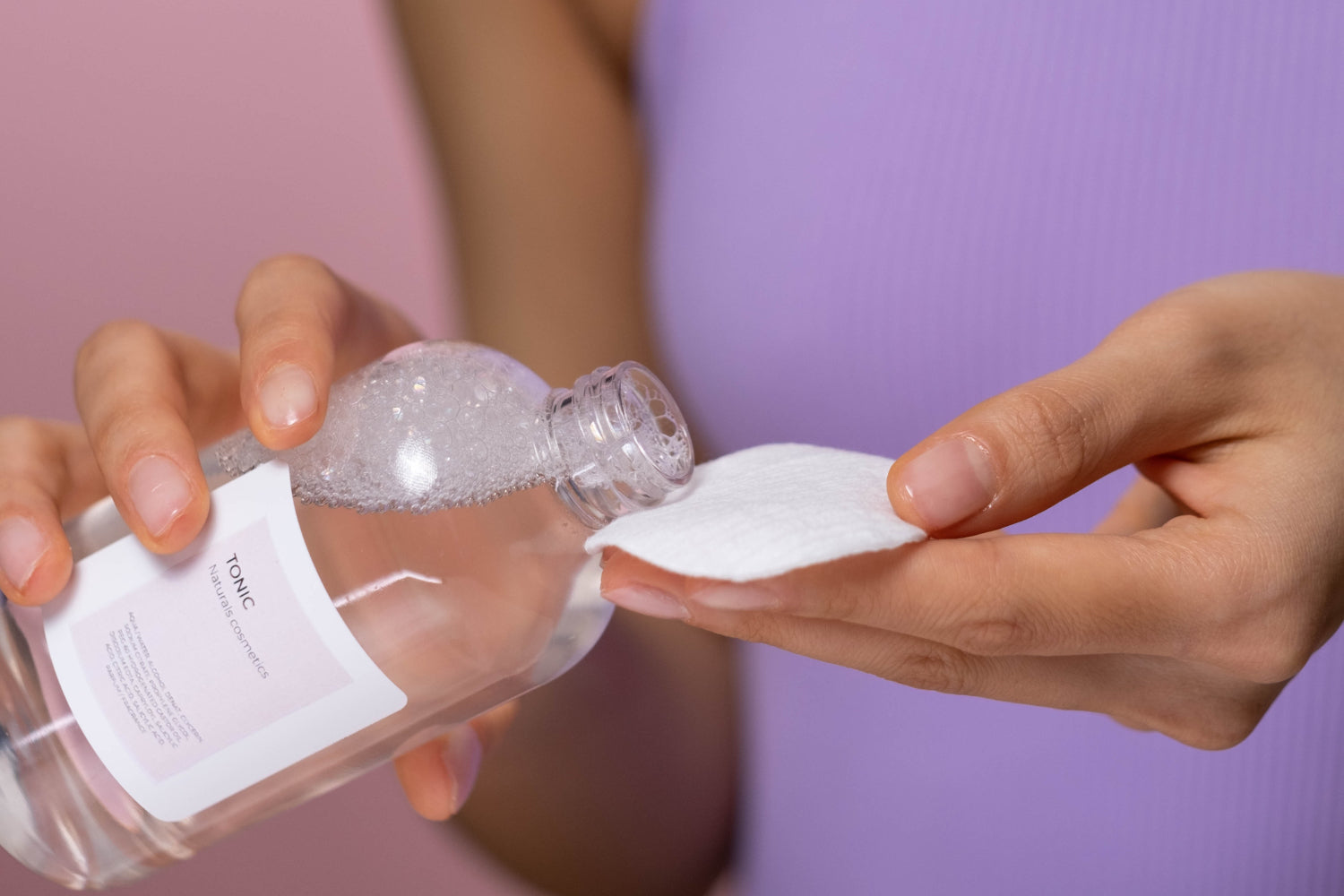 A person pours skin toner onto a cotton pad