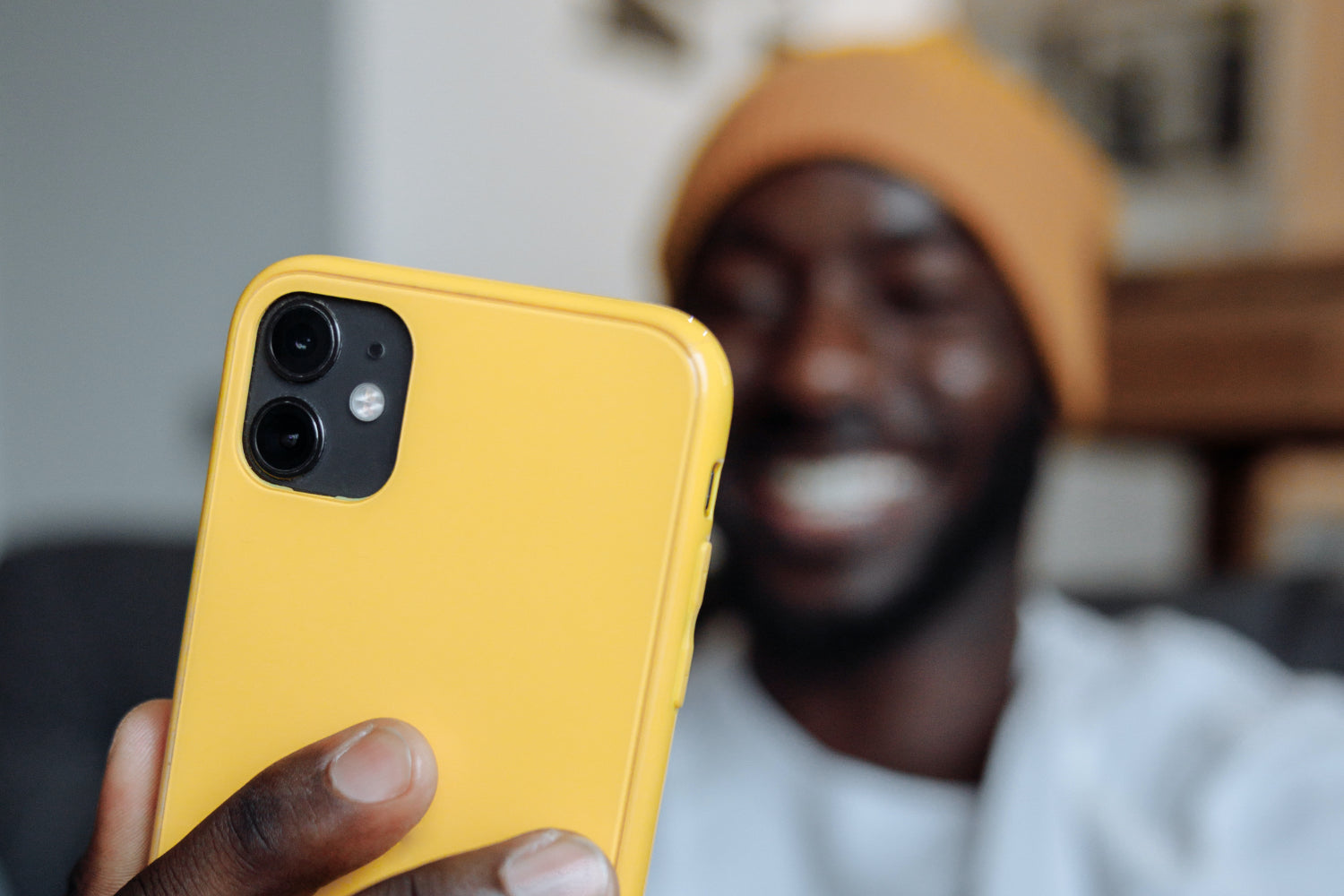 A man smiles while taking a selfie on a yellow mobile phone