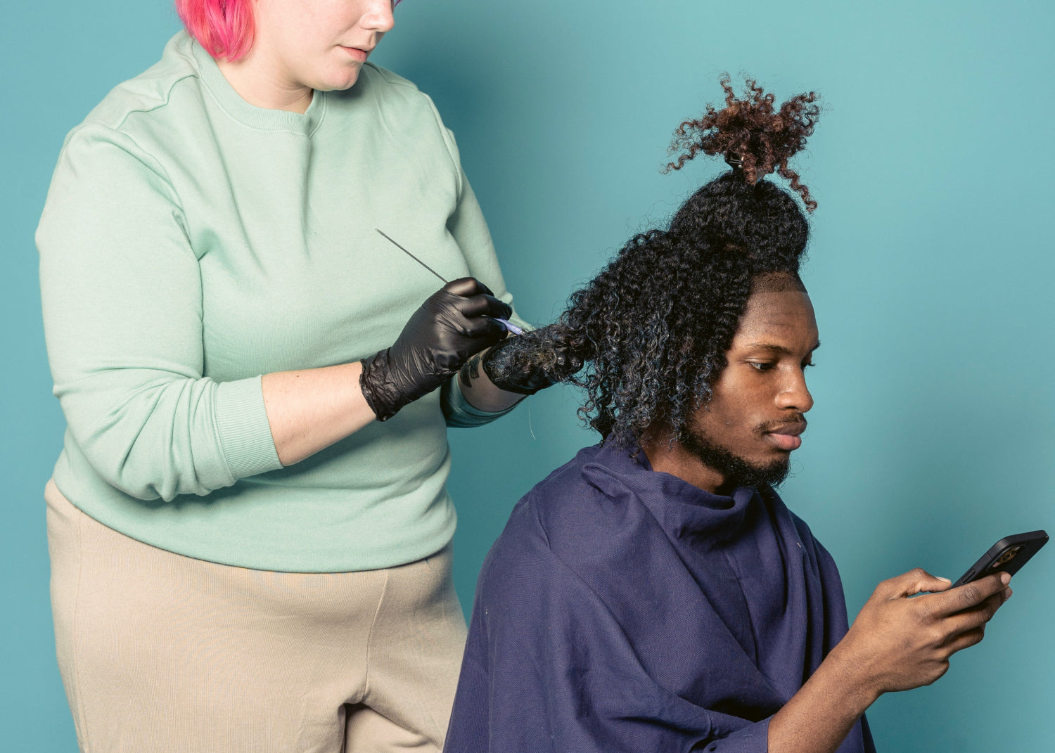 A person dyes the hair of another person who is sitting scrolling on a phone