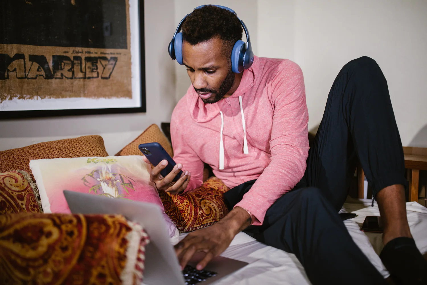 A man wearing headphones rests on a bed listening to music from a laptop