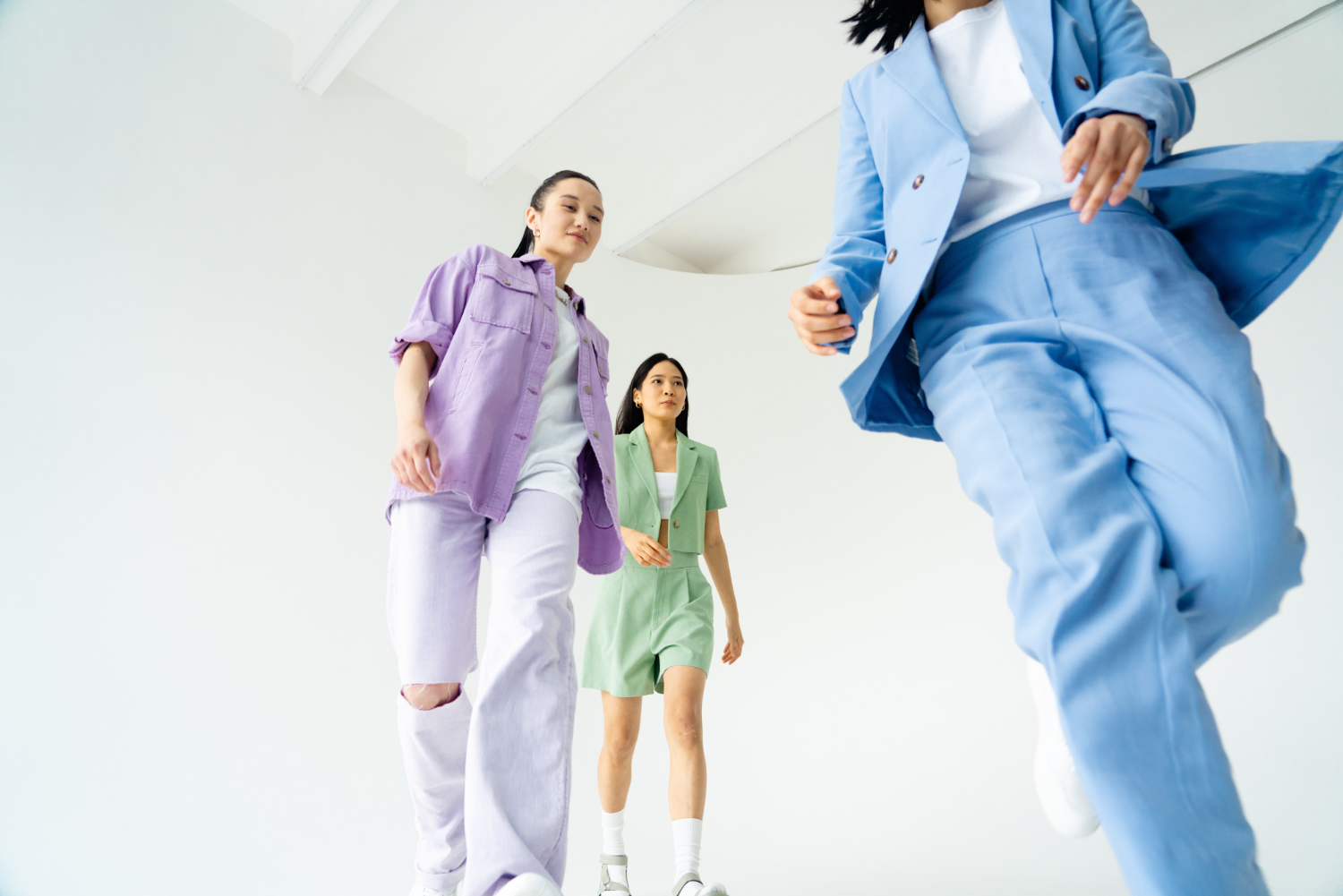 Three young women in pastel suits run in a white room