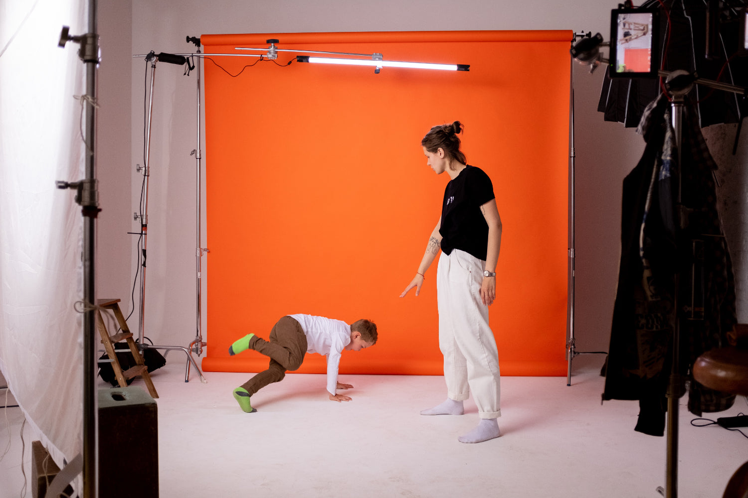 An adult and a child perform for the camera against an orange backdrop