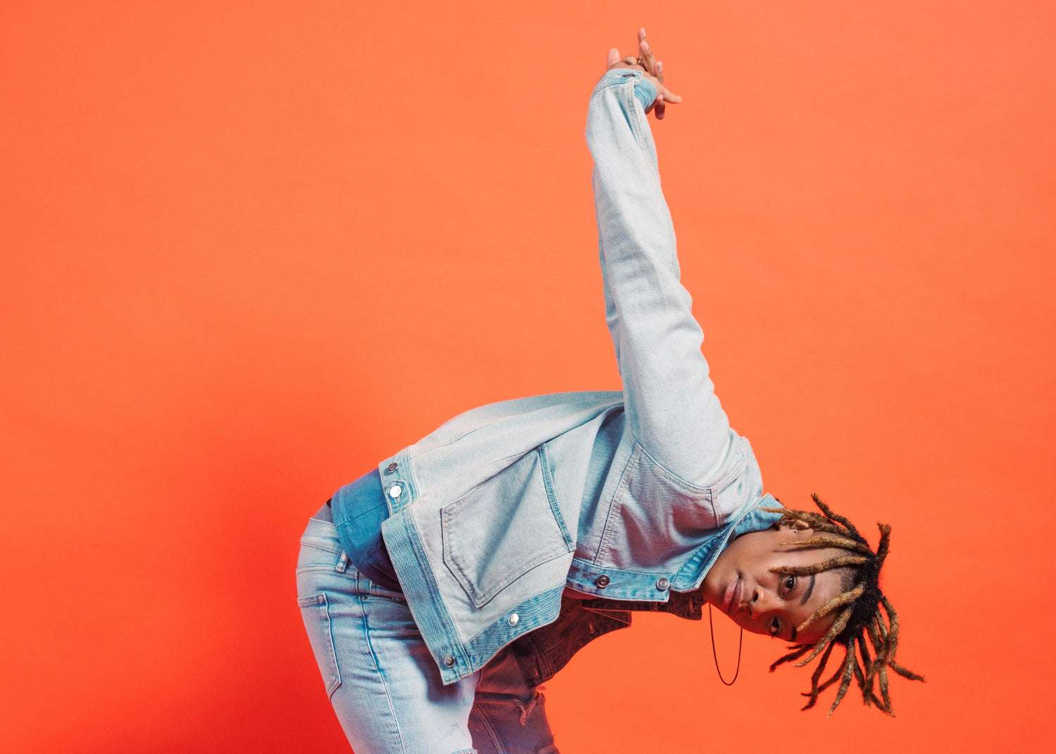 A man bends in half with his arms up against an orange background