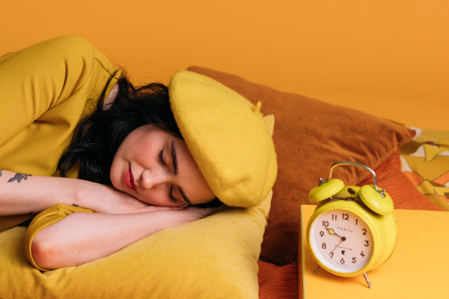 A woman in yellow sleeps next to a yellow alarm clock