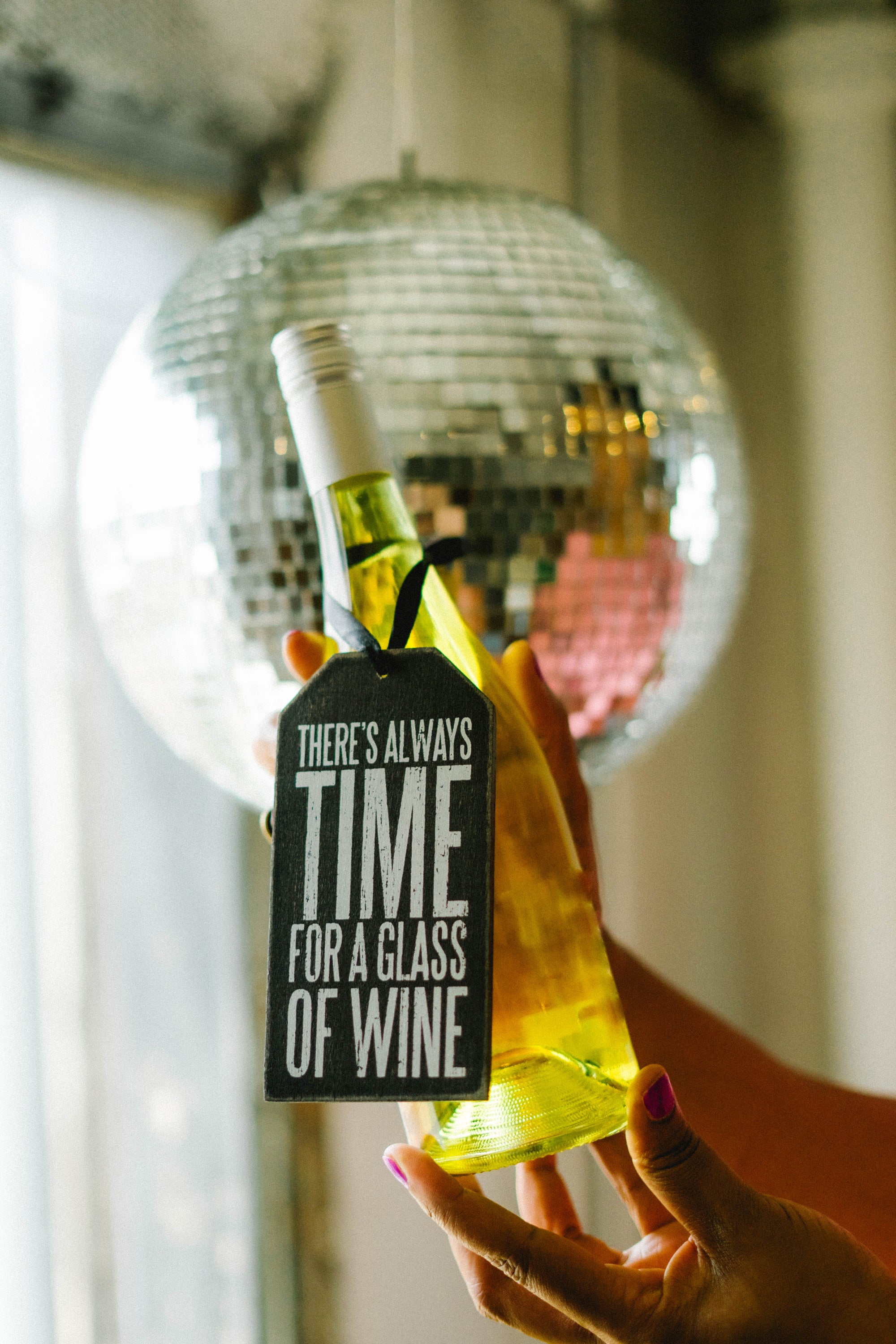 Felisha holds a bottle of wine in front of a disco ball