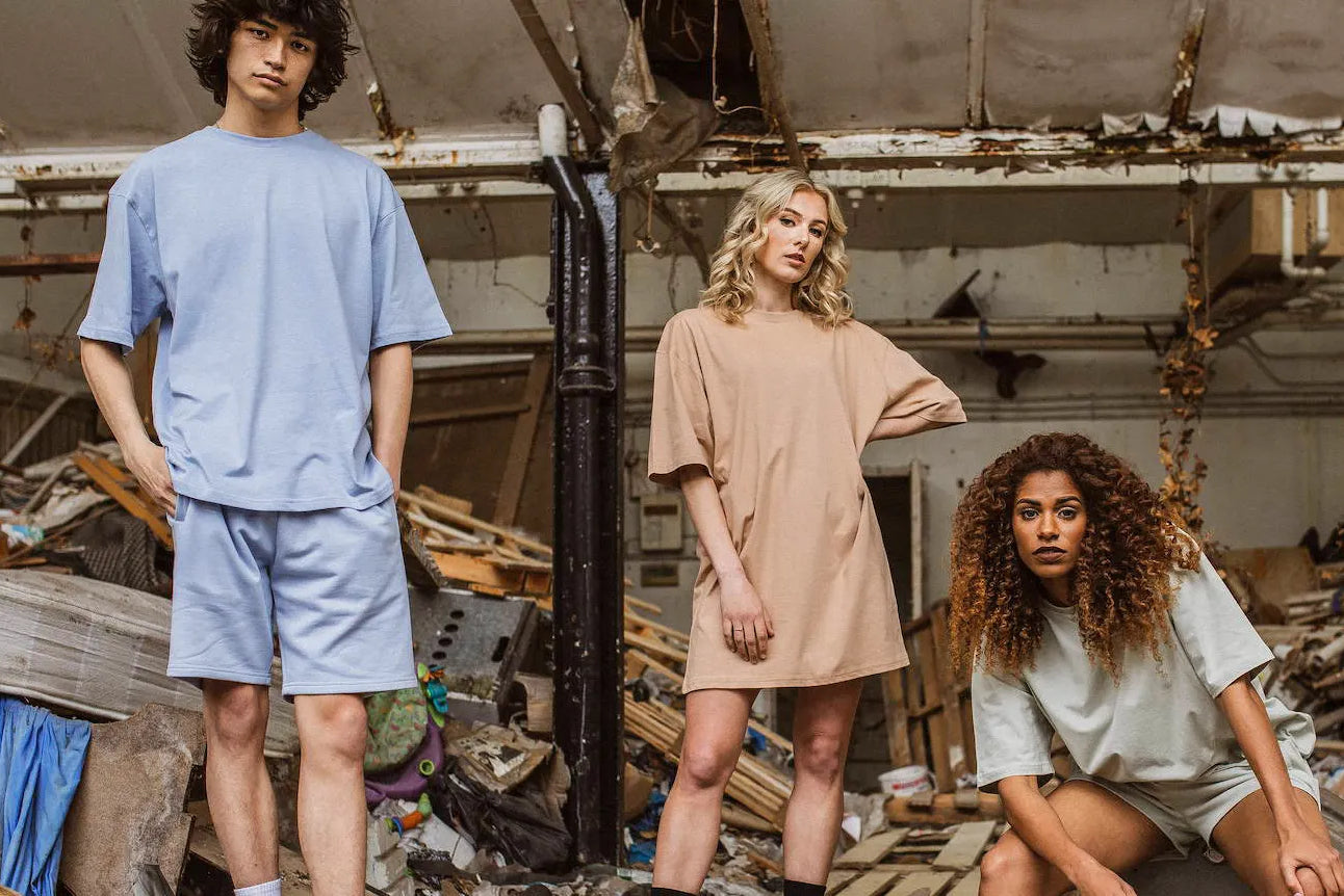 Three people model cotton clothing in a recycling facility