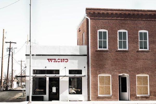 A white storefront with Wrong in red print next to a brick building.