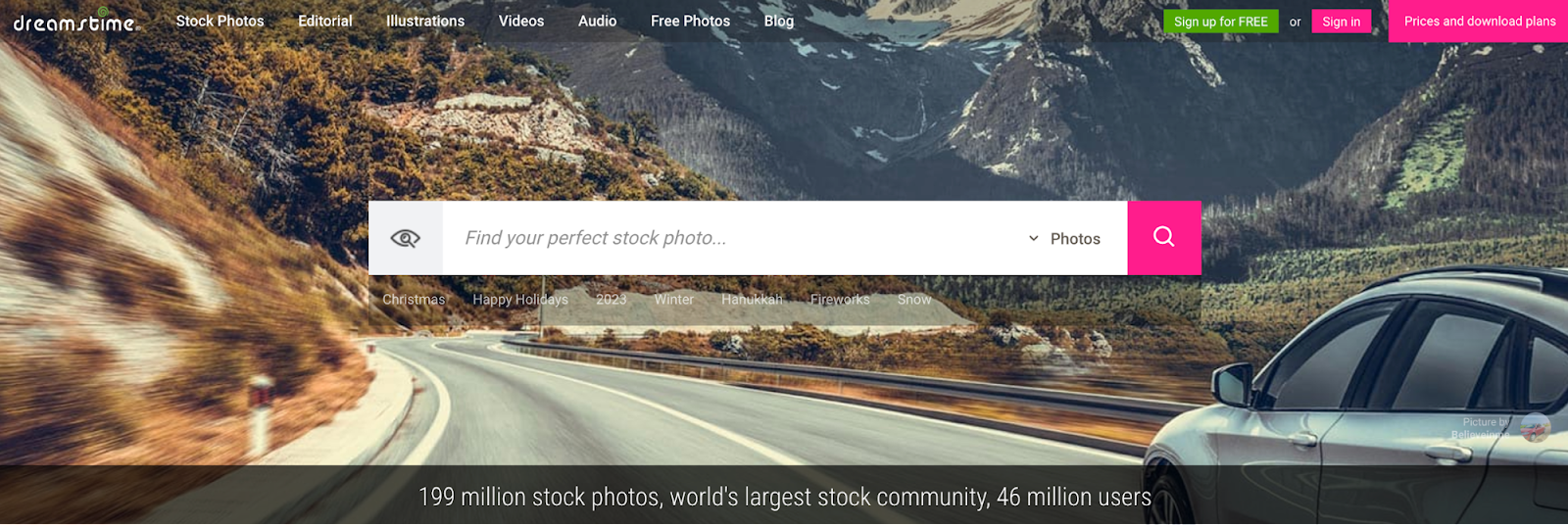 Dreamstime website with a photo search box overlaid on an image of a car driving through mountains.